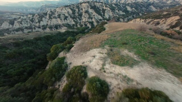 Fast FPV cruising drone shot over the hilly landscape of Calanchi di Aliano in Italy during sunset. 