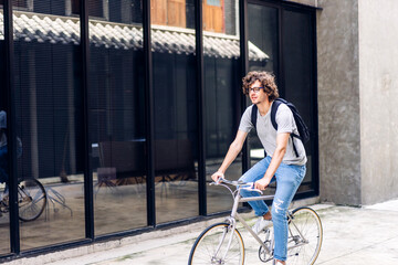 Obraz na płótnie Canvas Portrait of casual hipster handsome businessman with backpack looking forward while commuting riding bicycle on the street city way go to work.business travel transport bike concept