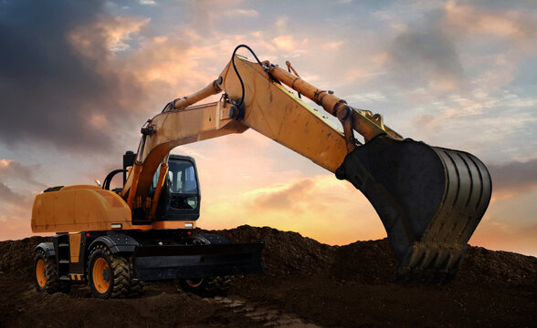 wheeled excavator at work digging soil during sunset.