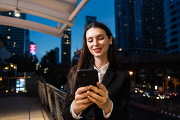 Caucasian businesswoman using mobile phone, working in city at night.