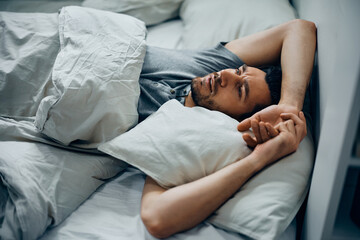 Thoughtful man lying down in bed.