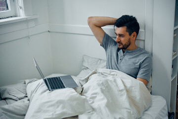 Mid adult man using laptop while relaxing in bedroom.