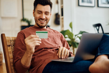 Happy man using laptop and credit card for online shopping at home.