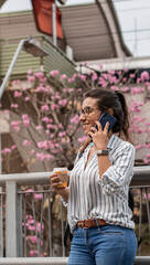Young businesswoman talking on the smartphone, drinking coffee walking around the business center. Concept of independent woman.