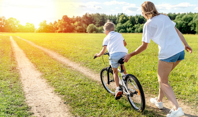 loving mother help her cute son ride a bicycle