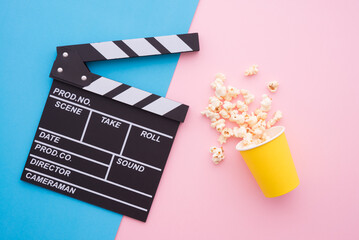 Cinema clapperboard and popcorn in paper bag on pink blue colorful background - Movie cinema entertainment concept.