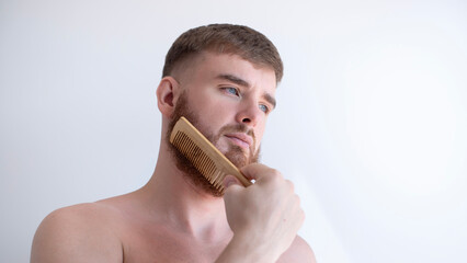 Handsome young bearded guy, European brutal man with a beard hair is combing the beard on face with...