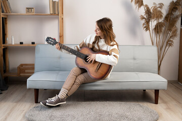 Pretty young woman playing guitar while sitting on sofa in the living room. Enjoying carefree time at home. Music is my life.