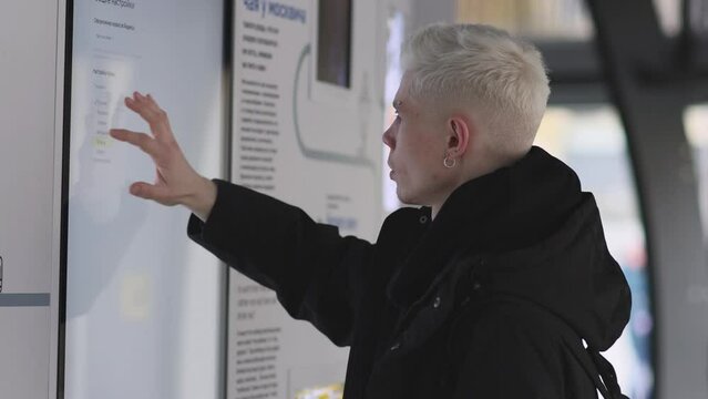 Male passenger analyzes transport card at a public transportation stop. Checking map and waiting for transport in city. Public transport route
