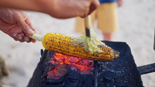 Cooking corn on a fire, Close-up, Man's hands hold a cob of corn over the fire, lubricates with oil. Slow motion