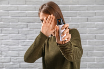 Young woman with pepper spray for self-defence on grey brick background