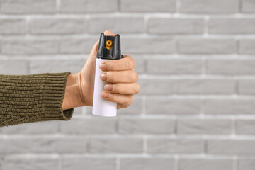 Young woman with pepper spray for self-defence on grey brick background, closeup