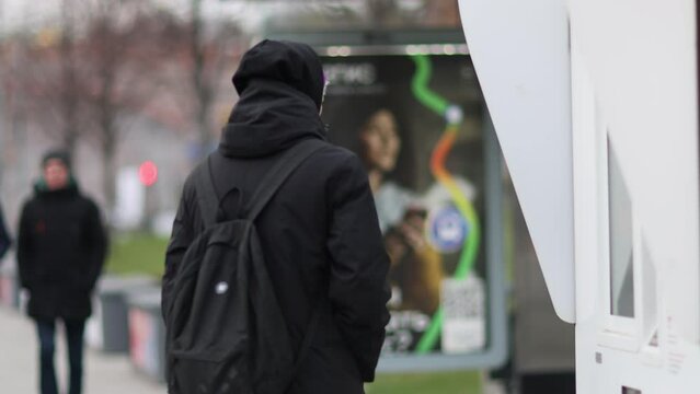 Male passenger analyzes transport card at a public transportation stop. Checking map and waiting for transport in city. Public transport route