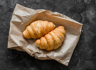 Fresh crispy croissants on a paper bag on a dark background, top view