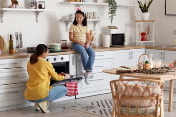 Little girl and her mother taking cupcakes from oven in kitchen on Easter day