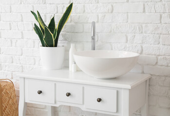 Naklejka na ściany i meble Table with sink, bath accessories and houseplant near white brick wall
