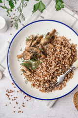 Plate of tasty buckwheat porridge with mushrooms and dill on grey table