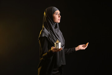 Praying Muslim woman with lantern on dark background