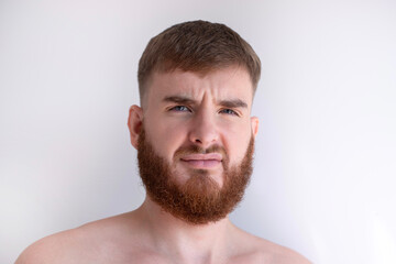 portrait of unhappy unsatisfied young bearded handsome man with beard is looking at camera on white...