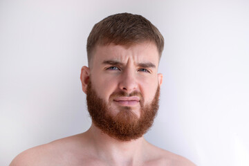 Obraz premium portrait of unhappy unsatisfied young bearded handsome man with beard is looking at camera on white background. 