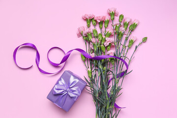 Bouquet of beautiful carnation flowers, ribbon and gift box on pink background. Women's Day celebration