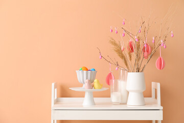 Vase with tree branches, Easter eggs and pampas grass on table near beige wall