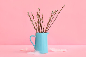 Jug with pussy willow branches and feathers on pink background