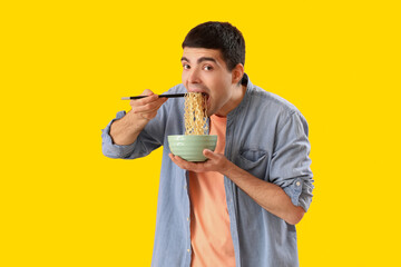 Young man eating Chinese noodles on yellow background