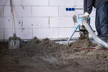 Semi-dry floor screed - a worker shovels a construction mixture through a special sleeve for cementing and leveling on underfloor heating pipes.