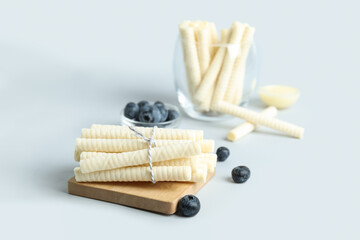 Board with stack of delicious wafer rolls tied by string on grey background