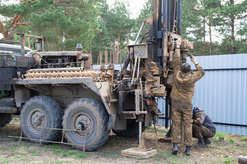 Team of workers with drilling rig on car are drilling artesian well for water in ground. Insertion...