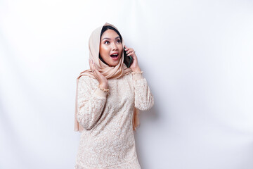 Shocked Asian woman wearing hijab, holding her phone, isolated by white background