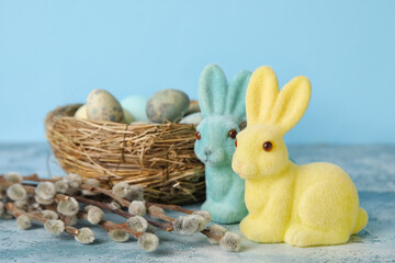 Easter bunnies, pussy willow branches and nest with painted eggs on grunge table against blue background