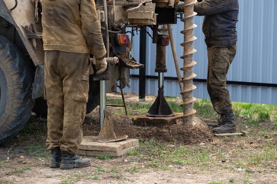 Team of workers with drilling rig on car are drilling artesian well for water in ground. Insertion of metal casing pipe into ground, installation of individual drinking supply