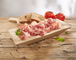 meat delicacy with tomatoes and bread on a wooden background. dry-cured pork on a tray. meat with a layer of fat under sunlight. traditional snack in rustic style.