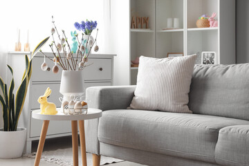 Vase with tree branches, Easter eggs and rabbit on table in interior of living room