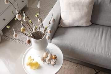 Vase with tree branches, Easter eggs and rabbit on table in living room