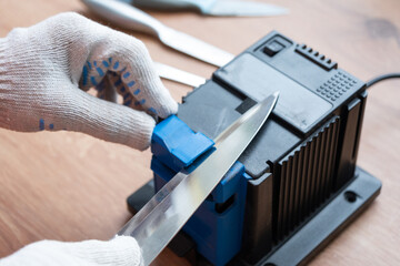 Sharpening a knife on an electric sharpener at home. The man's hand drives the knife blade between...