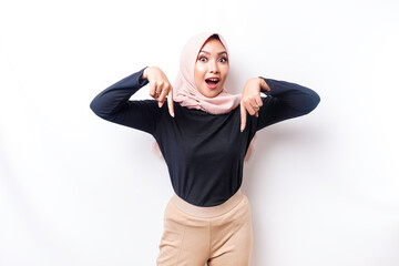 Shocked Asian Muslim woman wearing hijab pointing at the copy space below her, isolated by white background