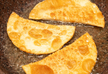 Pasties made from dough and minced meat are fried in oil in a frying pan.