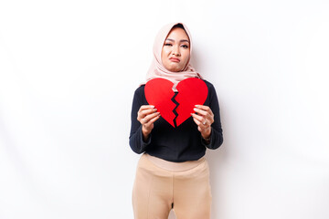 Beautiful young Asian Muslim woman expressed her sadness while holding broken heart isolated on white background