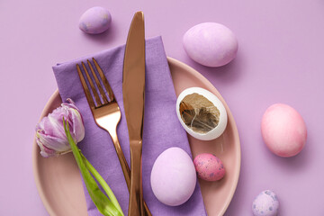Fototapeta na wymiar Table serving with Easter eggs and tulip flower on lilac background