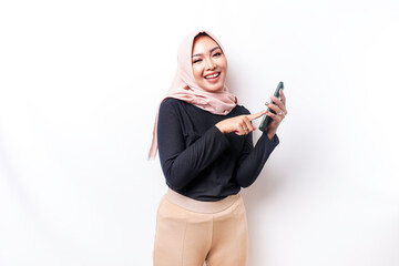 A portrait of a happy Asian Muslim woman wearing a hijab, holding her phone, isolated by white...