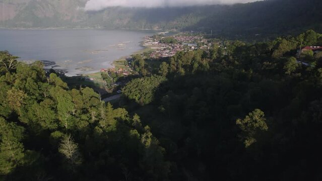Aerial shot in Bali flying over blue lake ata Mt Batur surrounded by fishertown and a forests on a mountain