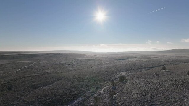 Vast snowy, frozen moorland and tundra lit by a low winter sun in a blue sky.