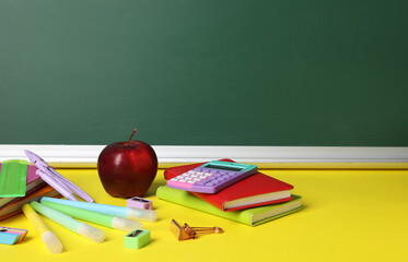 Different stationery and apple on yellow table against blackboard. Pi Day celebration
