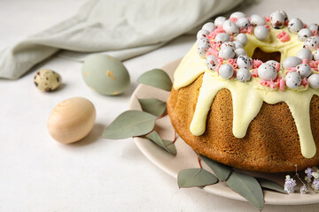 Plate with sweet Easter cake, eucalyptus branches and eggs on light table, closeup