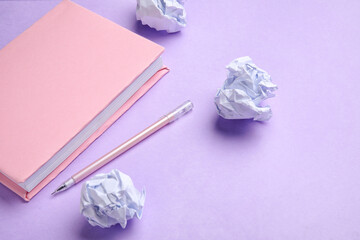 Book, pen and crumpled paper on lilac background. World Poetry Day celebration