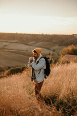 Enjoying the hilltop views. A male hiker looks aside with a smile on his face while standing on top of a hill with a backpack. Adventurous backpacker enjoying a hike at sunset.