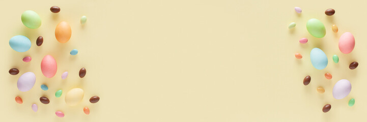 Happy Easter banner. Colorful Easter eggs and candies on the yellow background. Top view. Copy space.